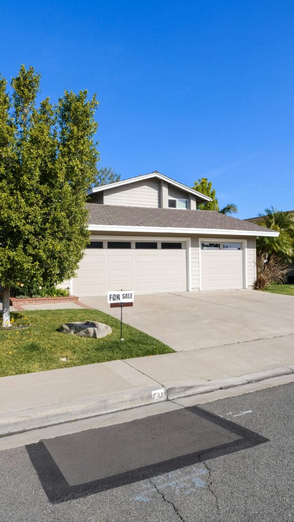 Suburban house with garage and For Sale sign in front yard against clear blue sky.